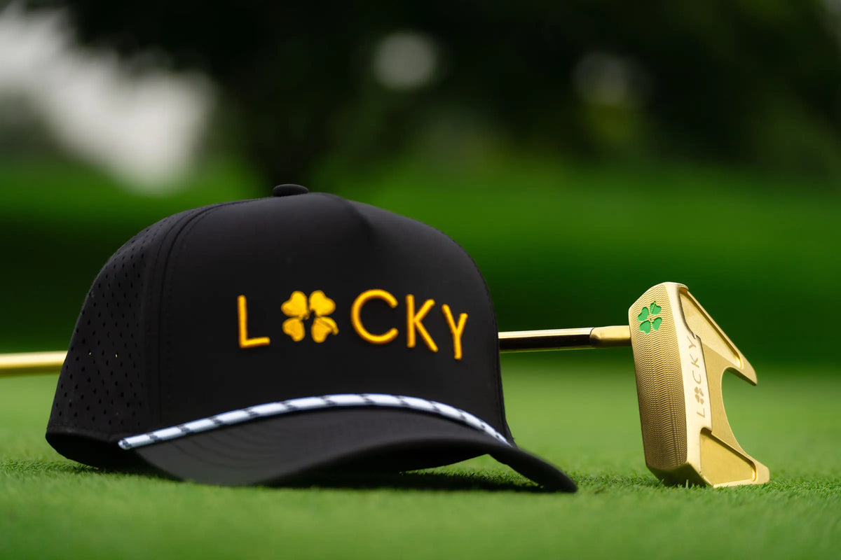 Black and gold Lucky hat on the green beside a gold mallet putter