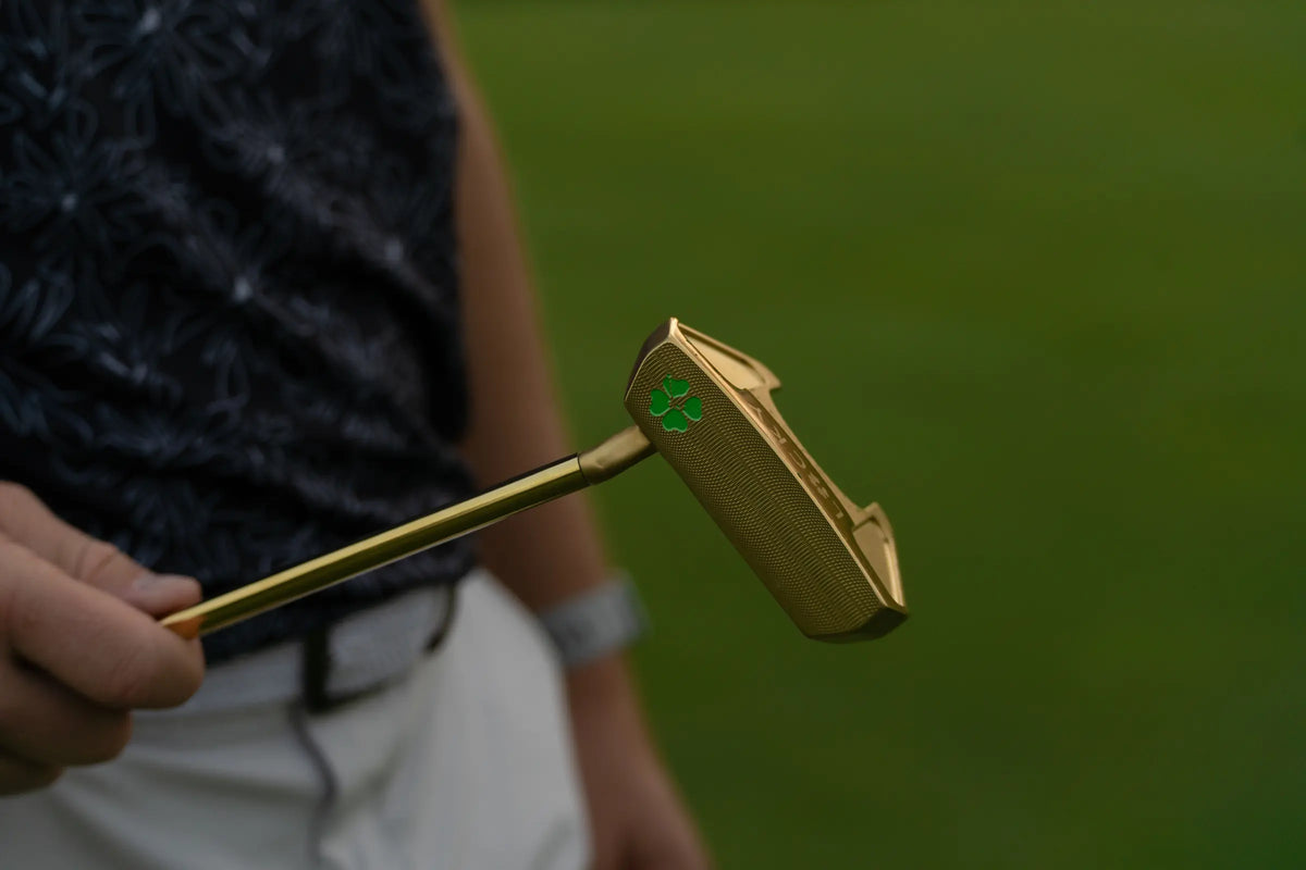 A gold blade putter held up against a Nightshade polo