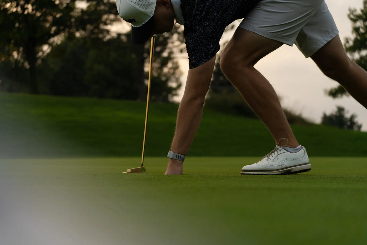 A golfer reaching into the cup, gold putter resting on the green