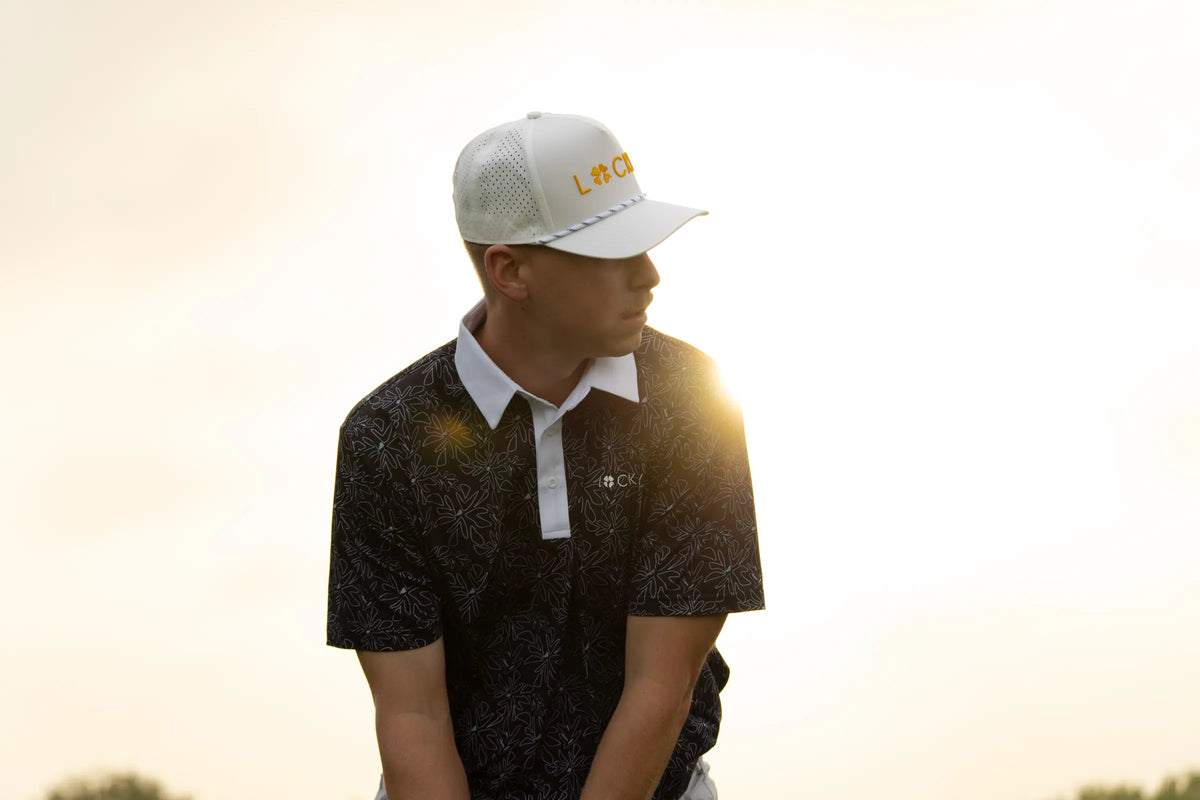 A golfer in a white Lucky hat and Nightshade polo in low sun